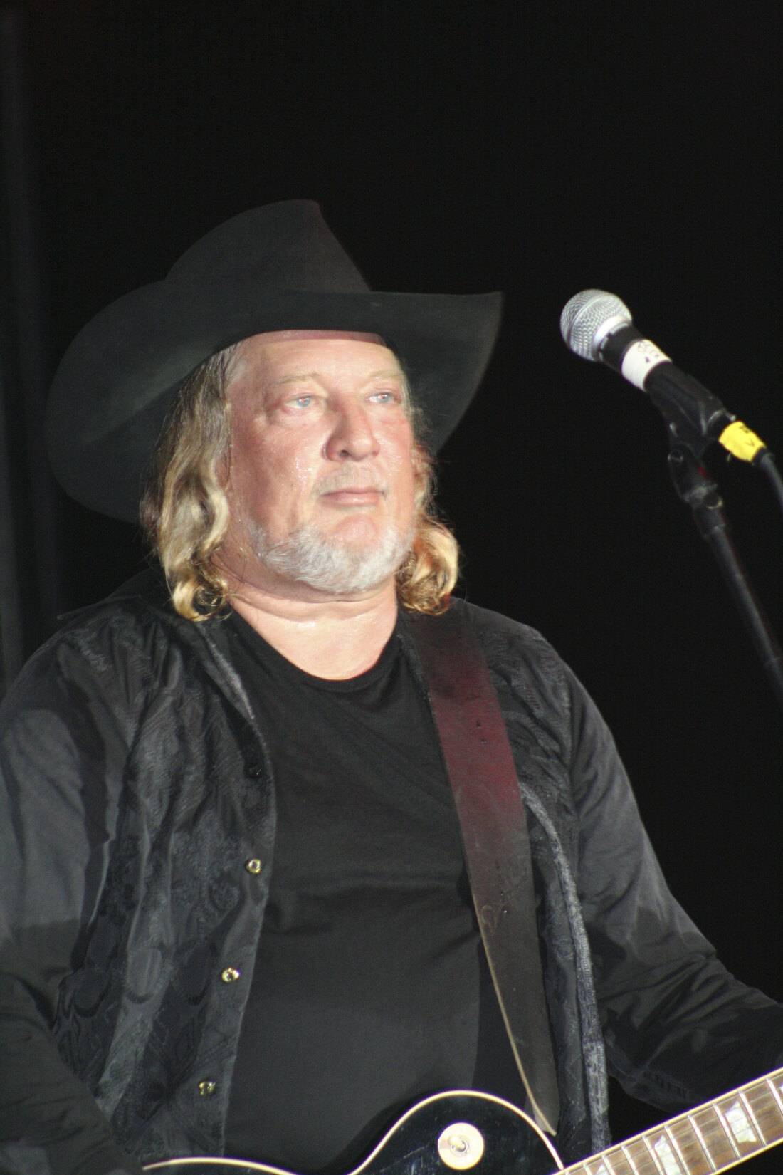 Country singer John Anderson in a black cowboy hat behind the microphone at the Pike County Fair in 2008, the Country Music Hall of Famer whose celebrity death at 71 was confirmed in October 2026
